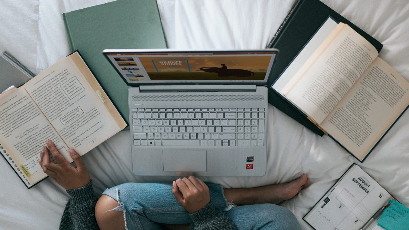 person in blue denim jeans sitting on bed with laptop
